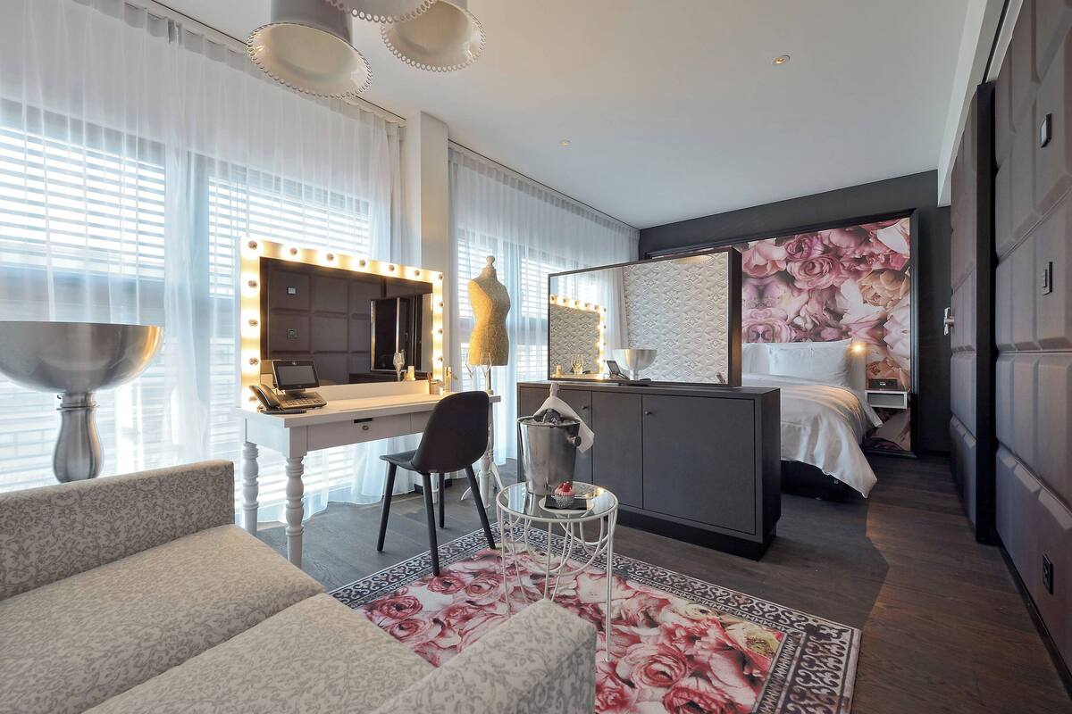 A hotel room with a vanity, mirror, and seating area.