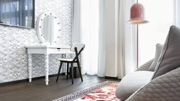 A modern bedroom with a white vanity, a large mirror, a grey sofa, and a floral carpet.