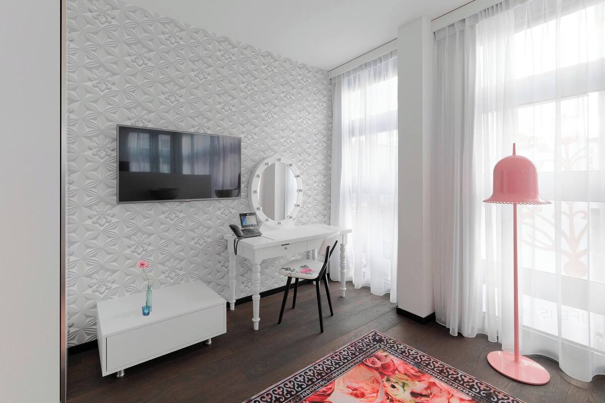A modern room with a white vanity, a flat-screen TV, a laptop, and a pink floor lamp.