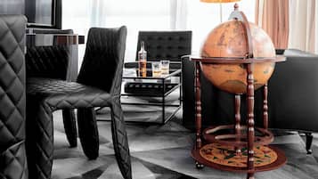 Een moderne hotelkamer met een zwarte leren bank, een houten wereldboltafel en een glazen salontafel.