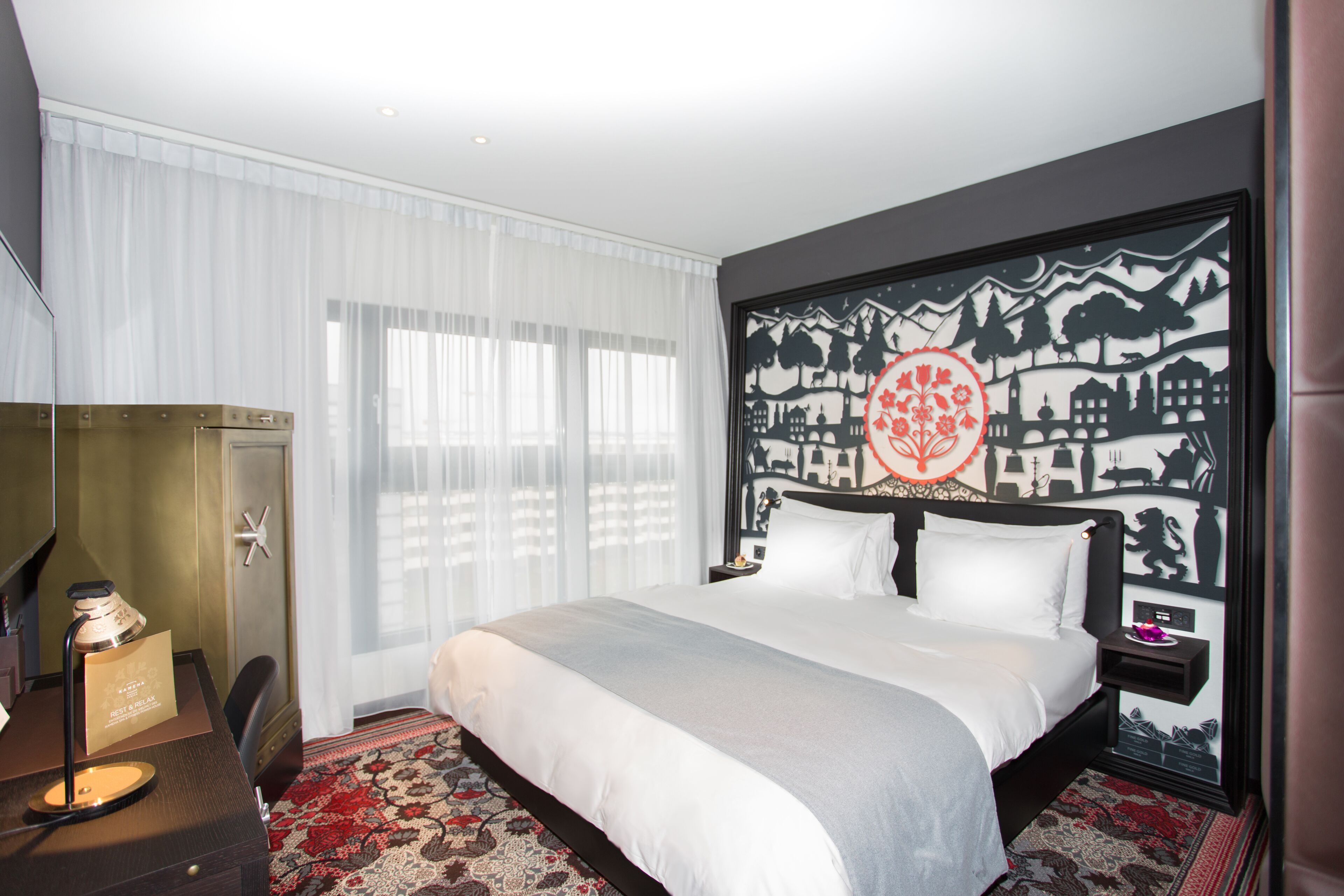 Une chambre d’hôtel avec un grand lit, un bureau avec une lampe et un mur orné d’un motif décoratif.