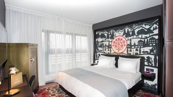 Une chambre d’hôtel avec un grand lit, un bureau avec une lampe et un mur orné d’un motif décoratif.