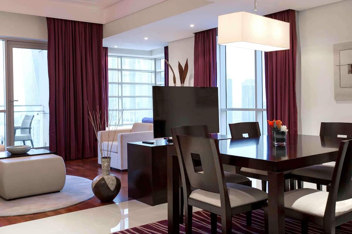 Ein modernes Hotelzimmer mit Essbereich, einer Couch, einem großen Fenster mit Vorhängen und Blick auf die Stadt.
