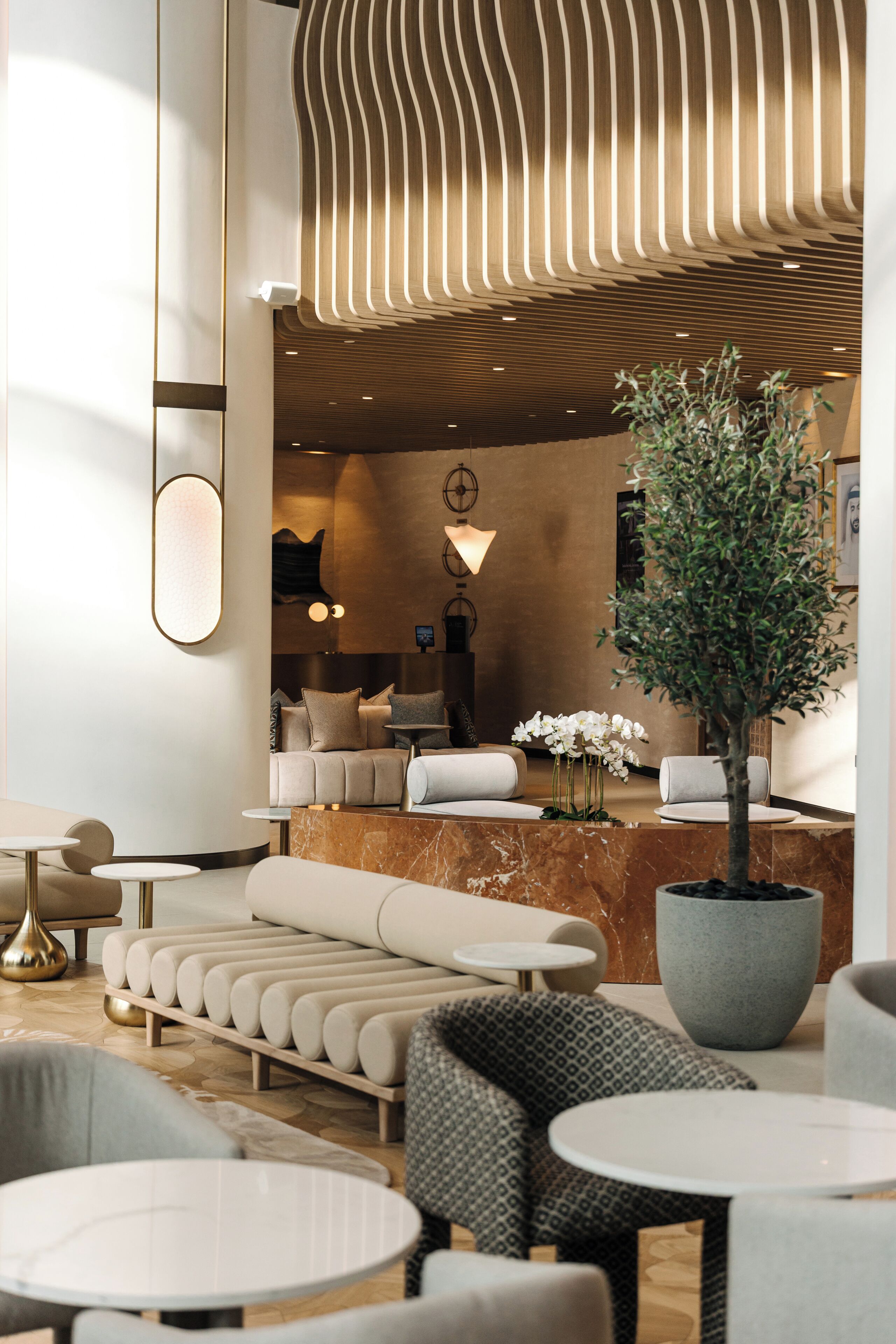 Un hall d’hôtel moderne avec un comptoir d’accueil, un espace salon et une grande plante en pot.