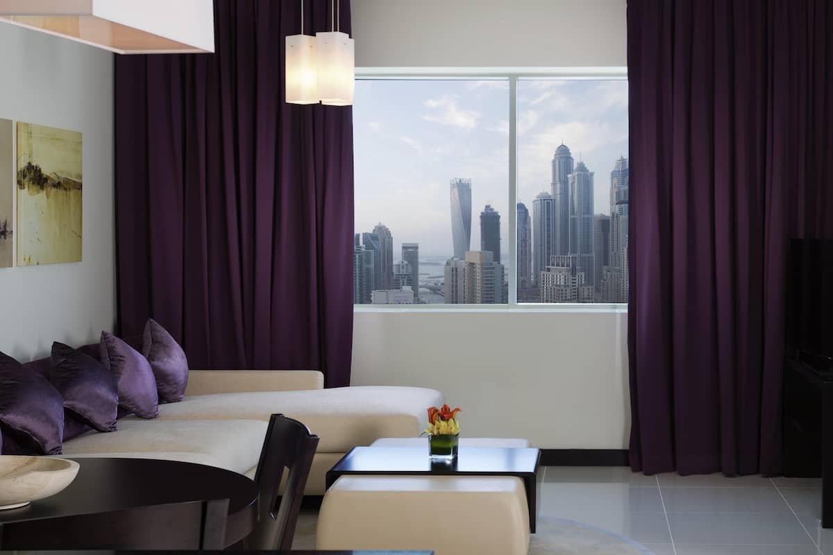 A modern hotel room with a city view, a bed, a dining area, and a TV.