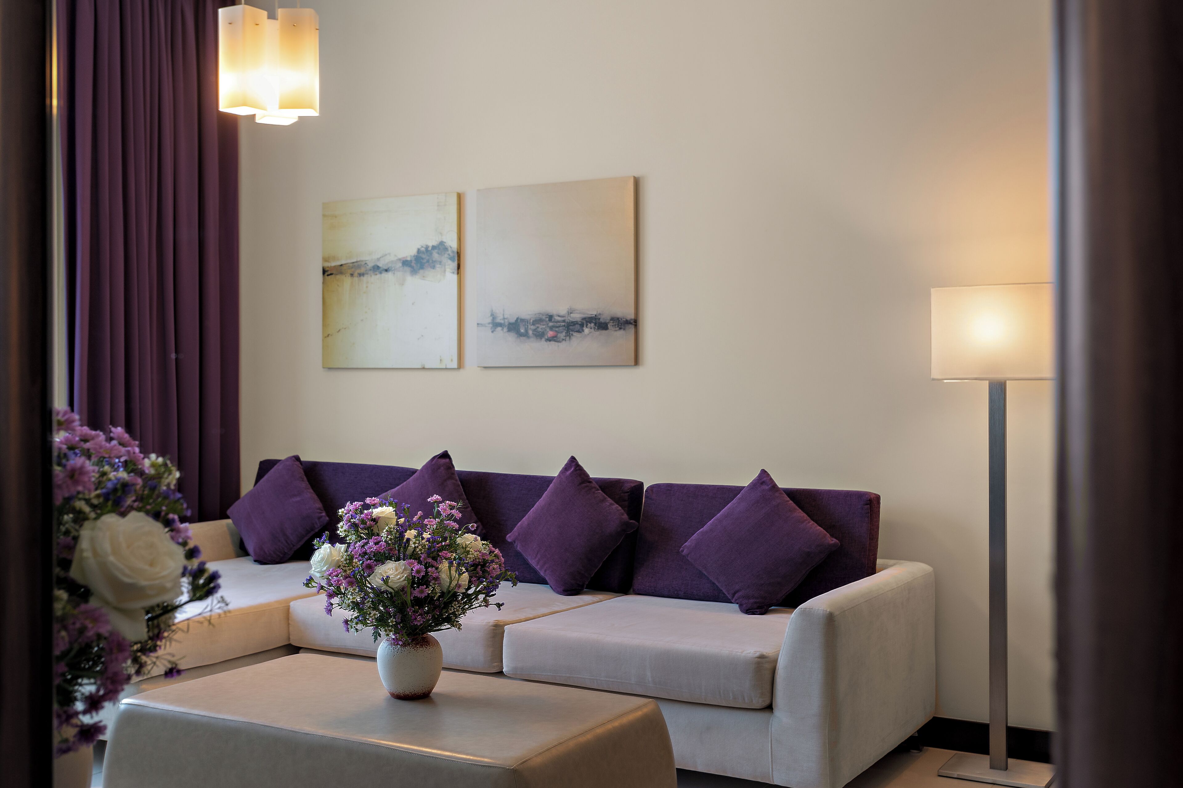 Ein modernes Wohnzimmer mit einer Couch, einem Beistelltisch mit Blumenvase und zwei an der Wand hängenden Bildern.