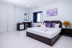 Una habitación de hotel moderna con una cama grande, un escritorio, una silla, una mesita de noche y un ventanal con cortinas.