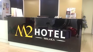 A reception desk at M2 Hotel Melaka with a modern design, featuring a black counter and a logo. - M2 Hotel Melaka (Malacca City)