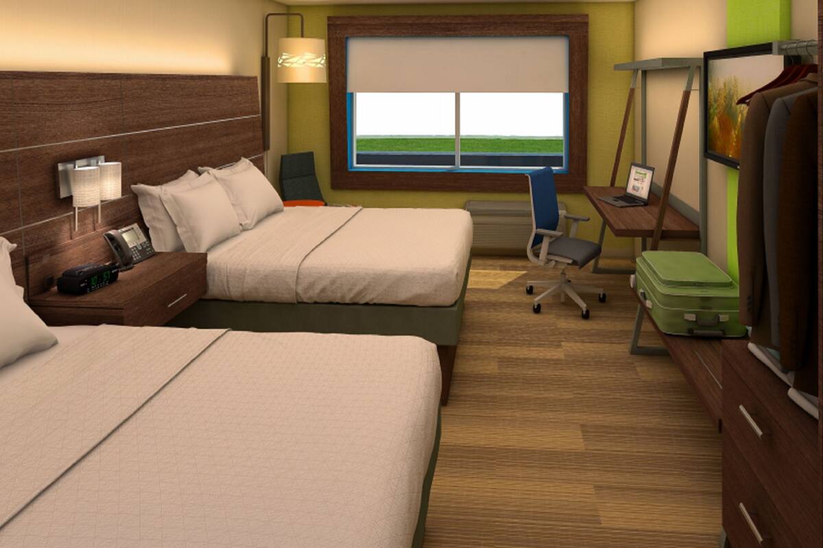 A hotel room with two beds, a desk, a chair, a TV, and a window with a view of the sky.