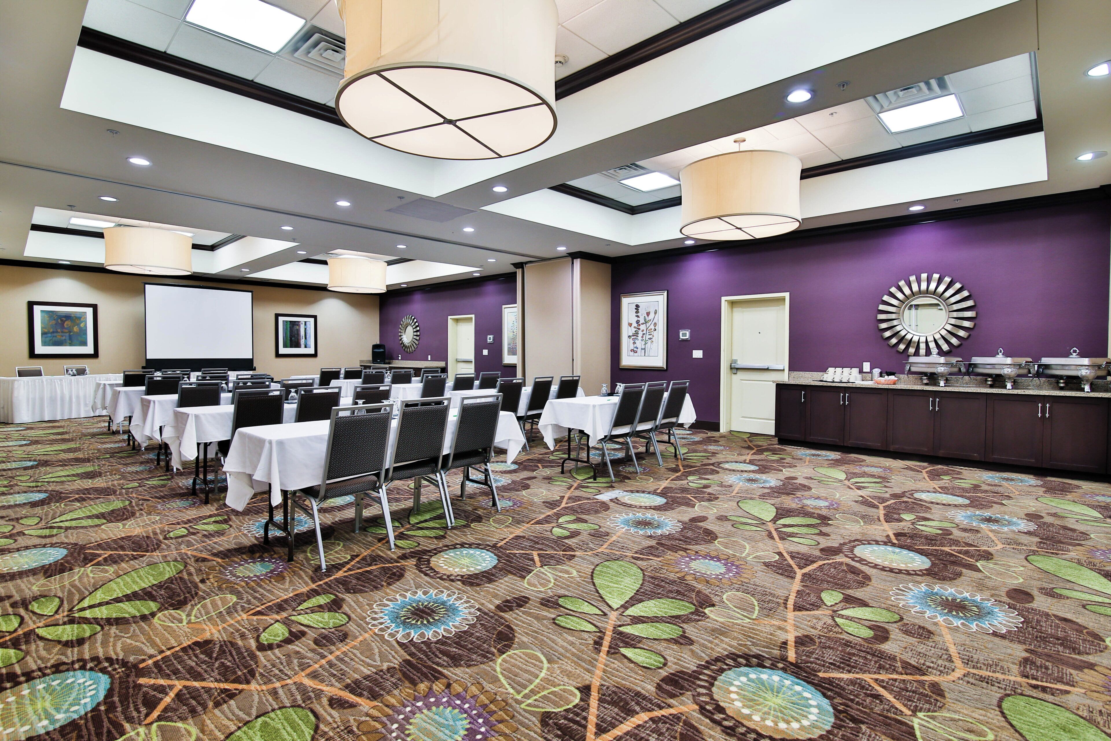 A conference room with tables and chairs, a projector screen, and a buffet area.