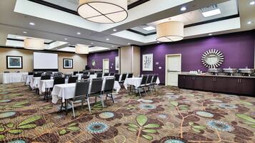 A conference room with tables and chairs, a projector screen, and a buffet area.