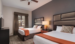 A hotel room with two beds, a television, a window with curtains, a ceiling fan, and a lamp.
