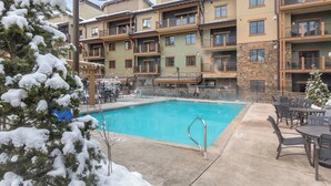 Ett poolområde med en klarblå pool, omgivet av utomhusmöbler och snötäckta träd.