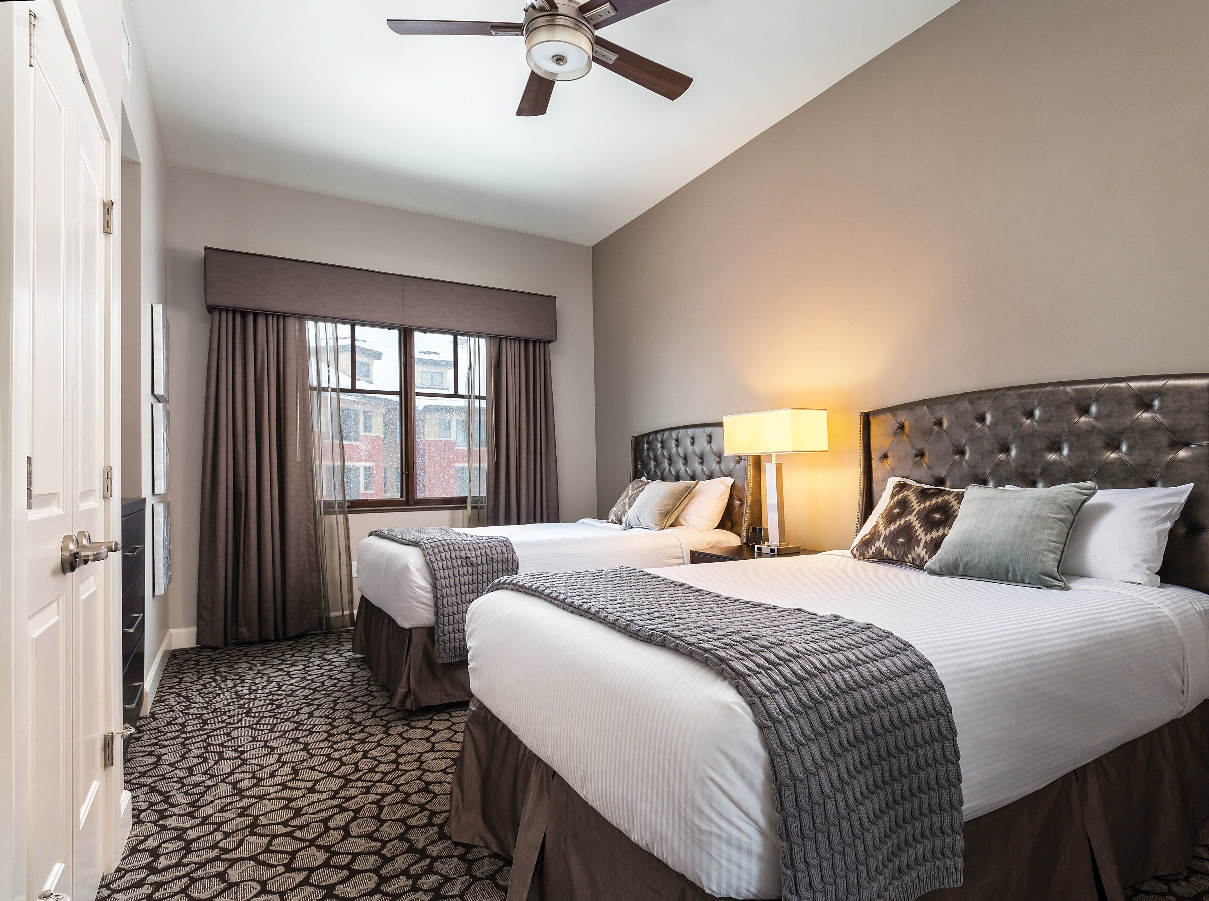 A hotel room with two beds, a ceiling fan, a window with curtains, and a patterned carpet.