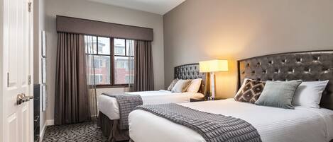 A hotel room with two beds, a ceiling fan, a window with curtains, and a patterned carpet.