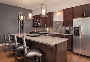 A modern kitchen with dark wood cabinets, a granite countertop, stainless steel appliances, and pendant lighting.