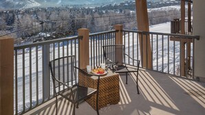 En balkong med två stolar och ett bord, med utsikt över ett snöklätt berglandskap.