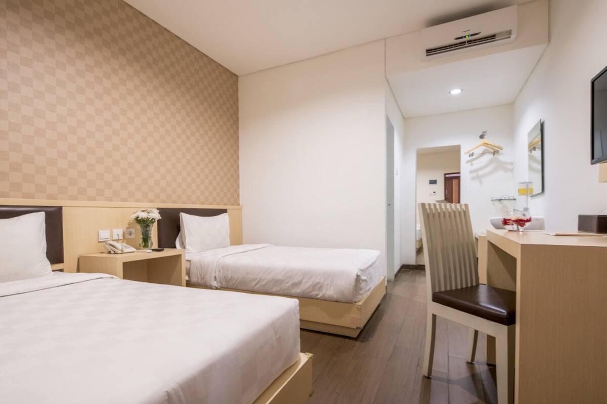 A hotel room with two beds, a desk, a chair, a mirror, and a wardrobe.