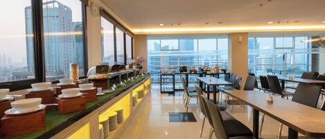 A modern dining area with a buffet setup, large windows, and a view of the cityscape.