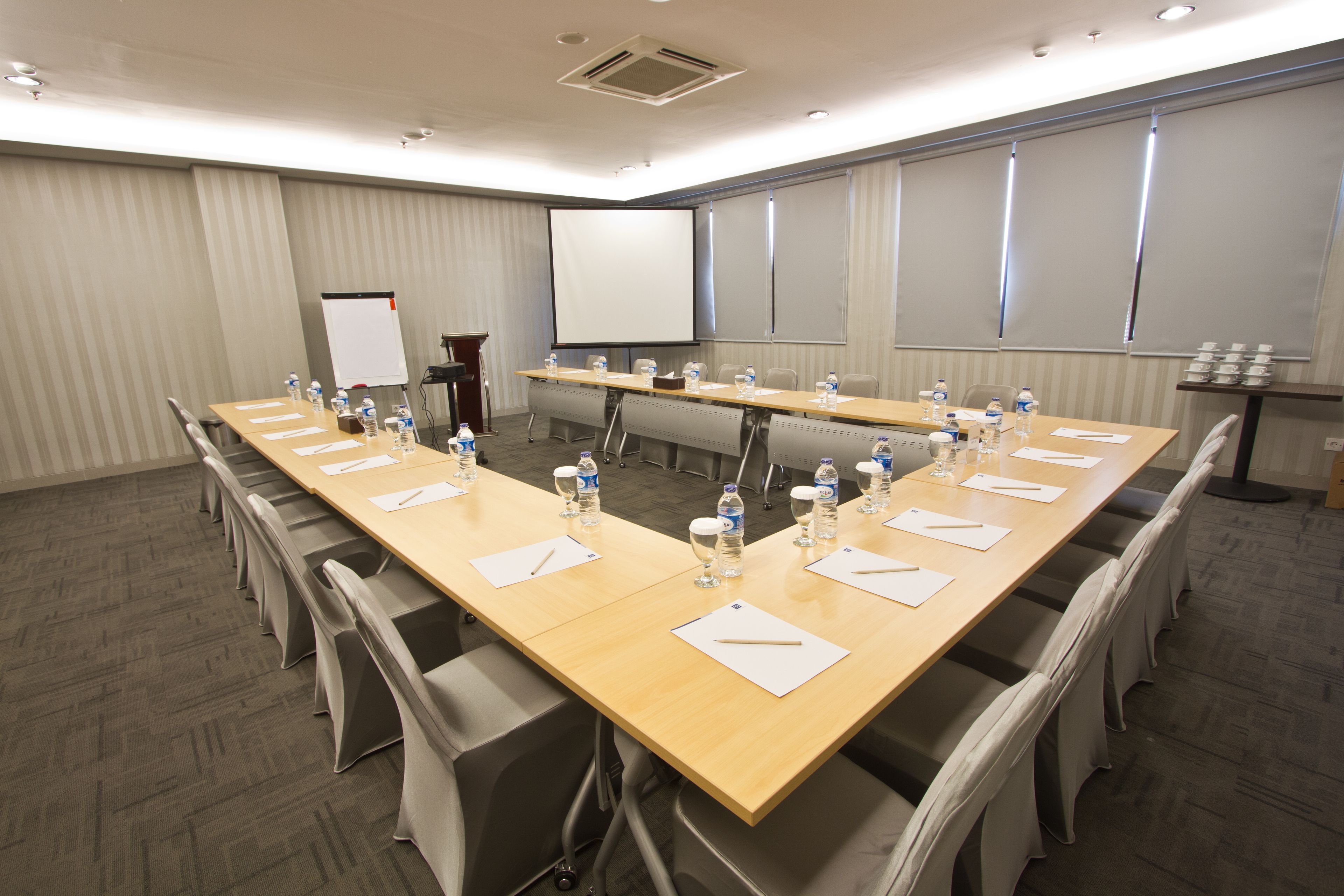 Un salón de conferencias con una larga mesa, sillas, botellas de agua y una pantalla para proyector.