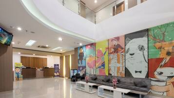 A modern hotel lobby with a reception desk, seating area, and a large mural on the wall.