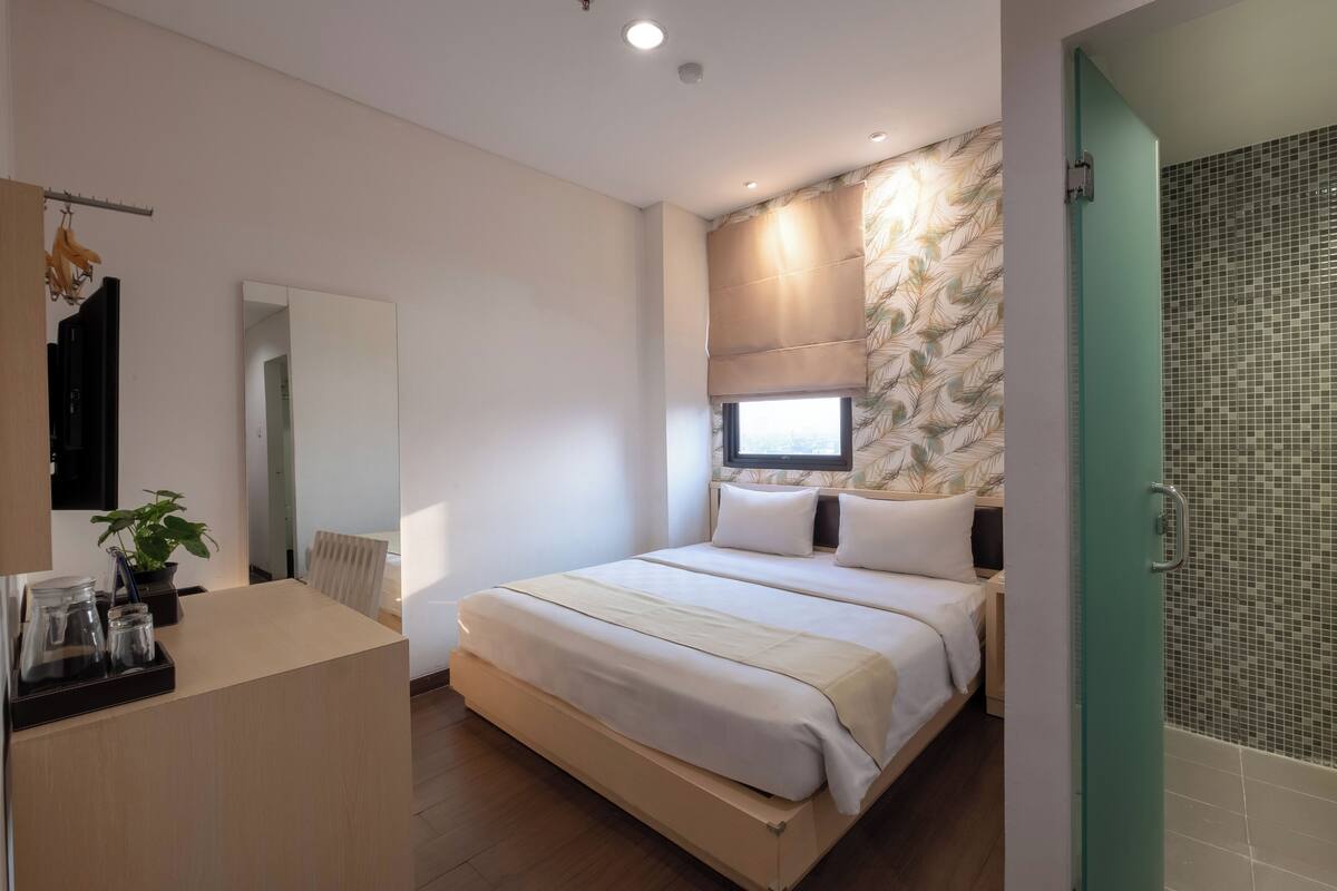 A modern bedroom with a large bed, bedside tables, a mirror, and a shower area.