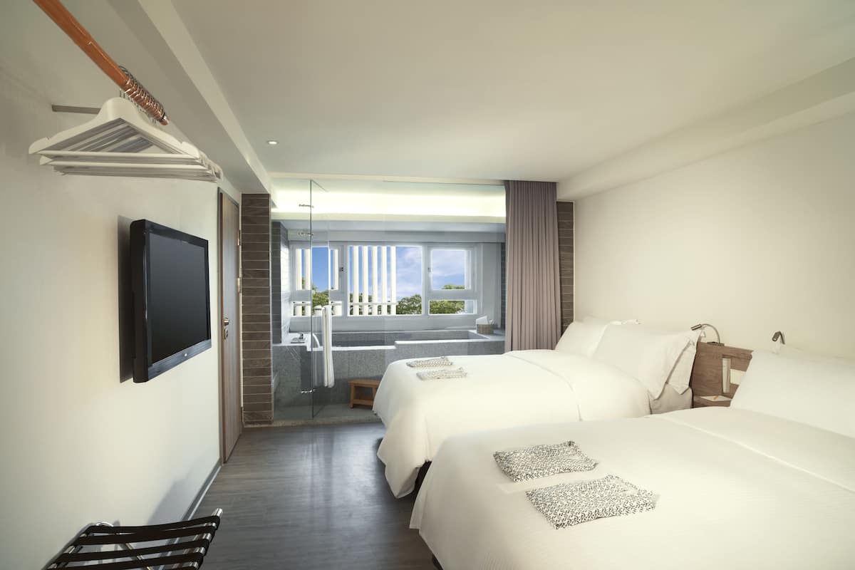 A modern hotel room with two beds, a TV, a balcony with a view, and a small seating area.