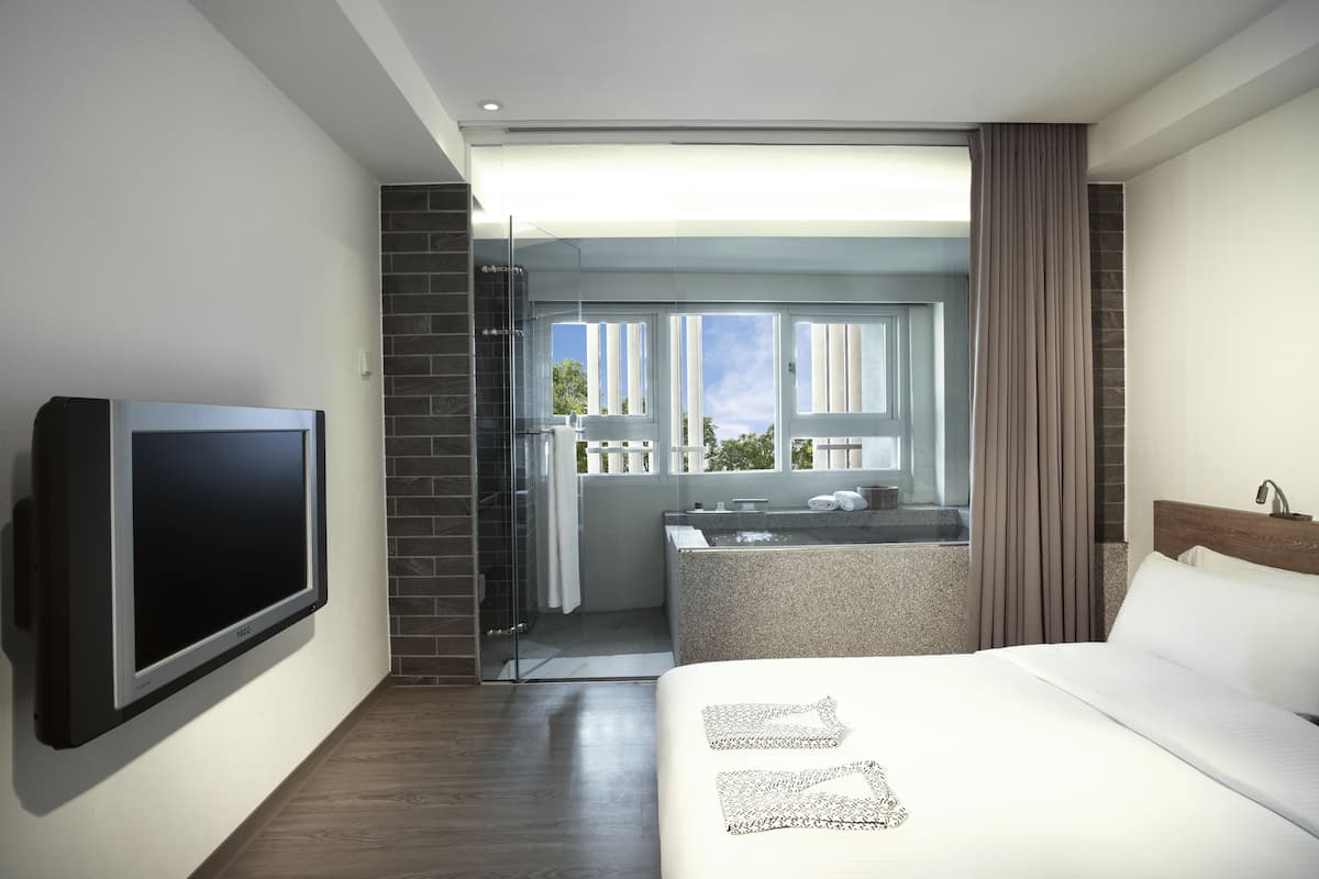 A modern hotel room with a large bed, a flat-screen TV, a bathroom with a bathtub, and a balcony with a view.
