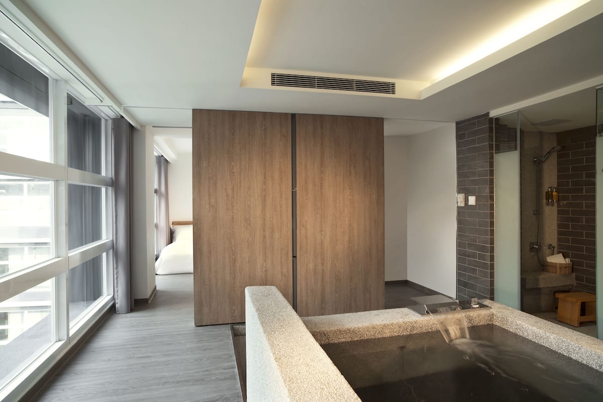 A modern bathroom with a large window, a wooden wardrobe, a bathtub, and a shower area.