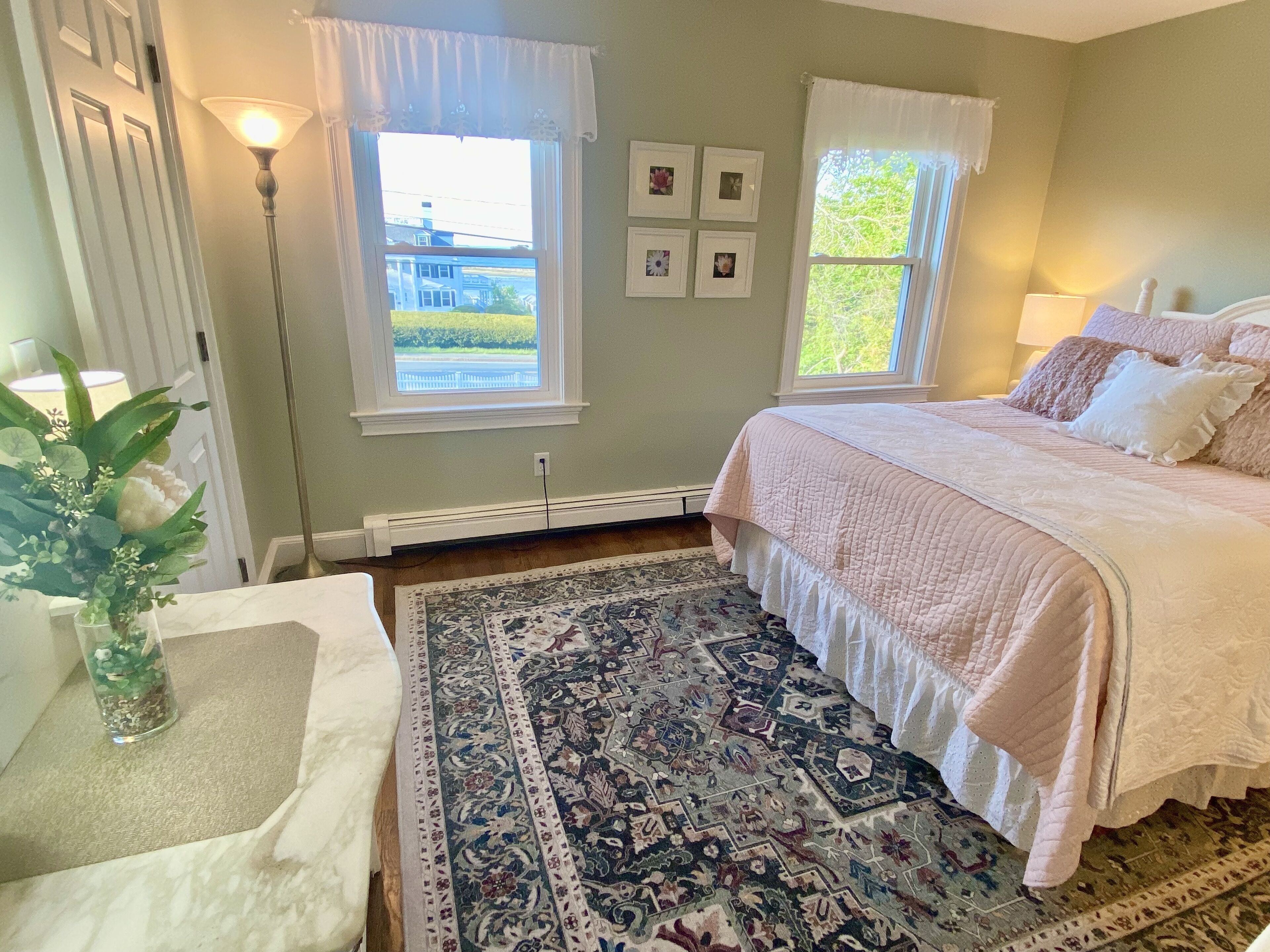 A bedroom with a bed, a rug, a lamp, and a window with a view.