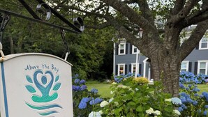 A sign for '3 Waves Wellness Retreat' with a heart-shaped logo, surrounded by lush greenery and hydrangea flowers. - 3 Waves Bed & Breakfast (Plymouth)