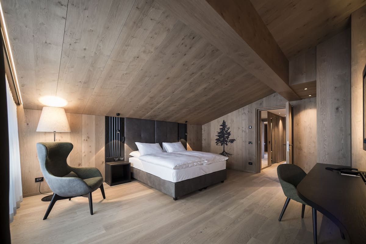 A modern bedroom with a wooden ceiling, a large bed, two chairs, a desk, and a nightstand.