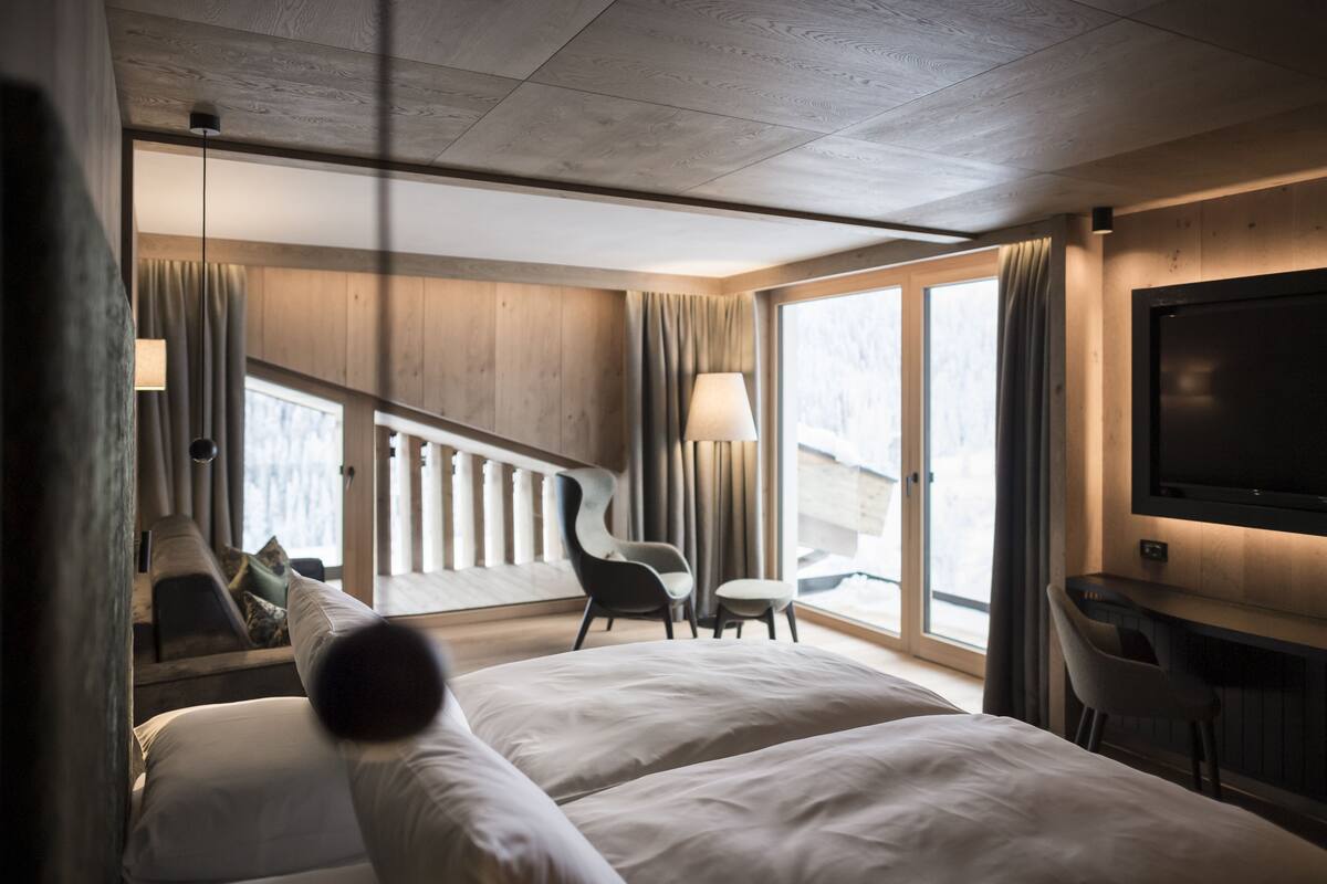 A hotel room with a large bed, a desk, a chair, and a TV. There is a staircase leading to an outdoor area.