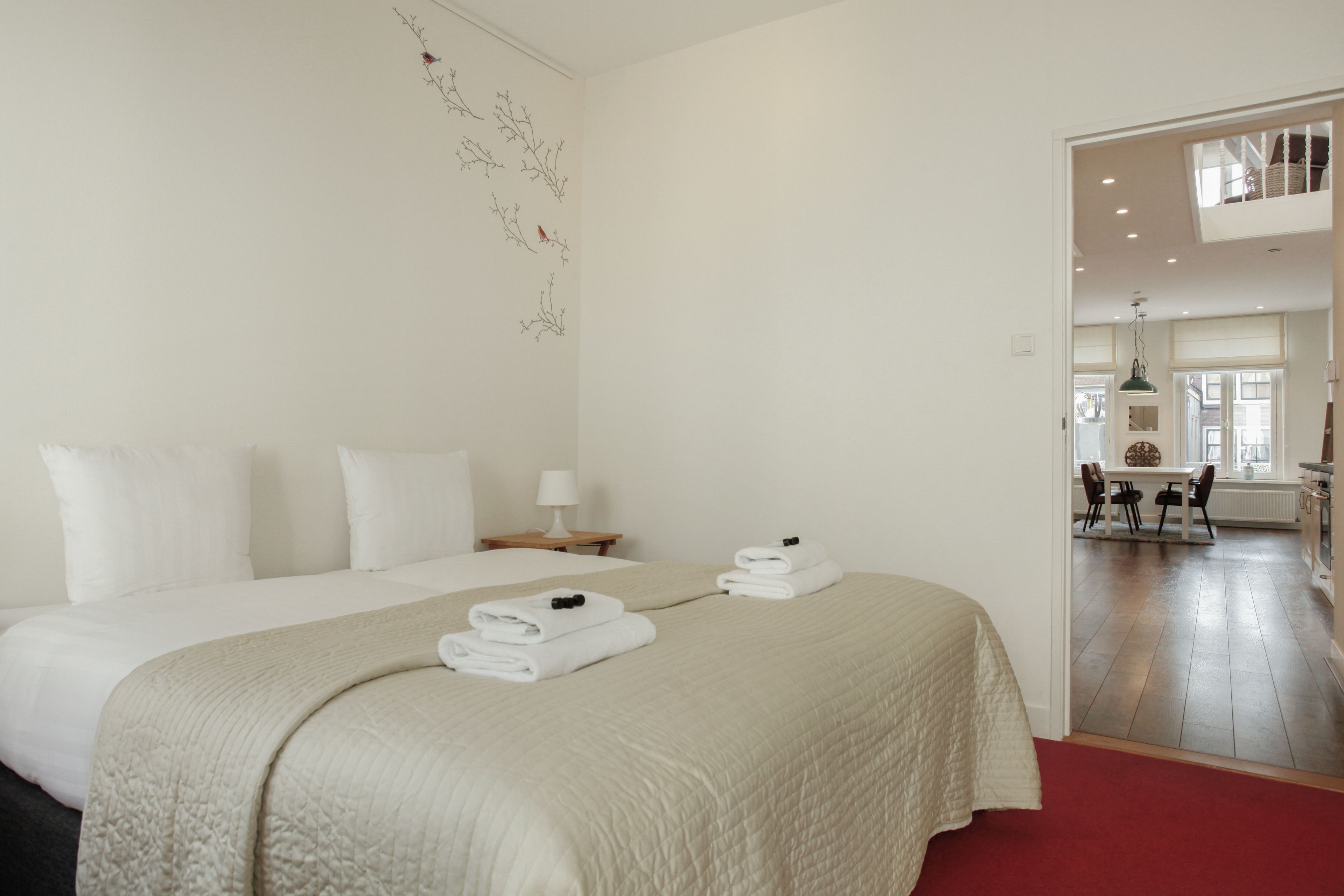 A hotel room with a large bed, a nightstand, a lamp, and a view of the dining area.