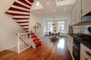 A spacious kitchen with wooden flooring, a central island, and a staircase with red steps.