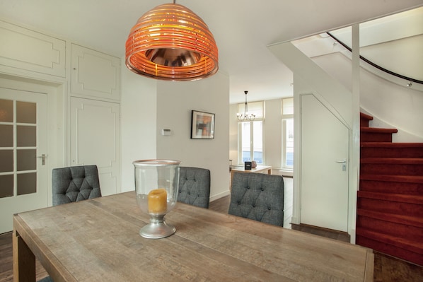 A dining area with a wooden table, four upholstered chairs, a clear glass candle holder, and a copper pendant light.