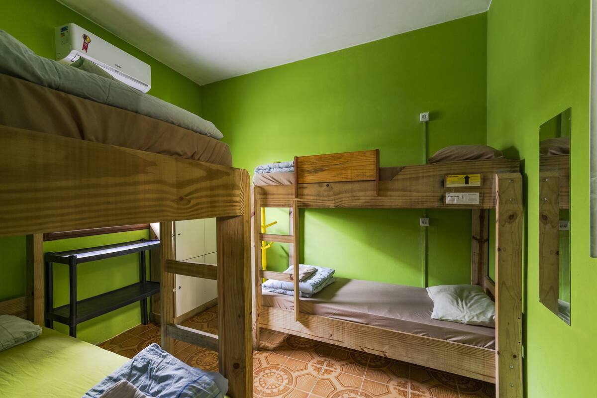 Ein Schlafsaalzimmer mit Etagenbetten, einem Regal und einer Wand-Klimaanlage.