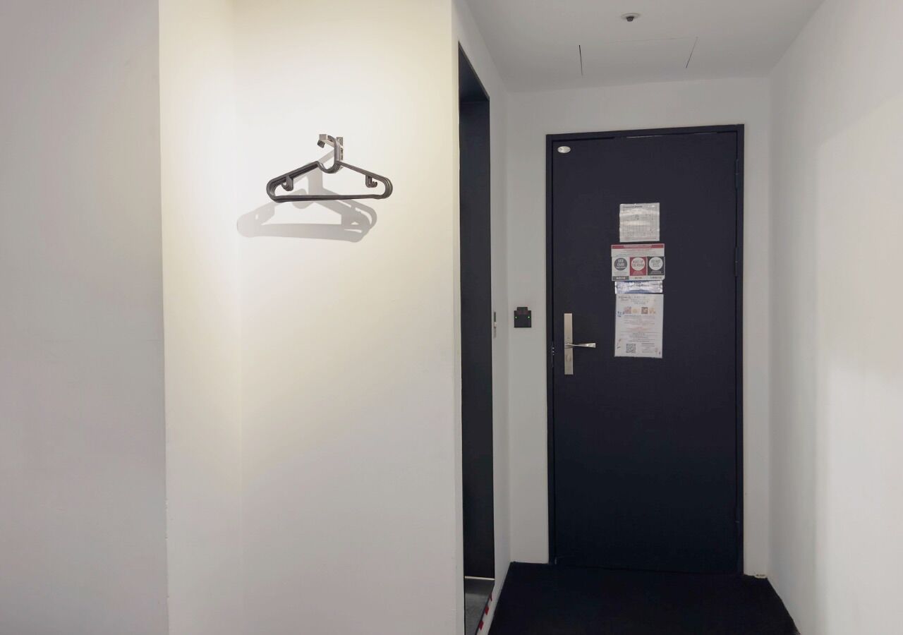 A hallway with a coat rack, a black door with a notice, and a small step leading to the door.