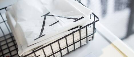 Un panier en métal rempli de sacs blancs, qui contiennent peut-être du linge, est posé sur une surface où l’on peut voir un texte relatif à une machine à laver et à un sèche-linge.