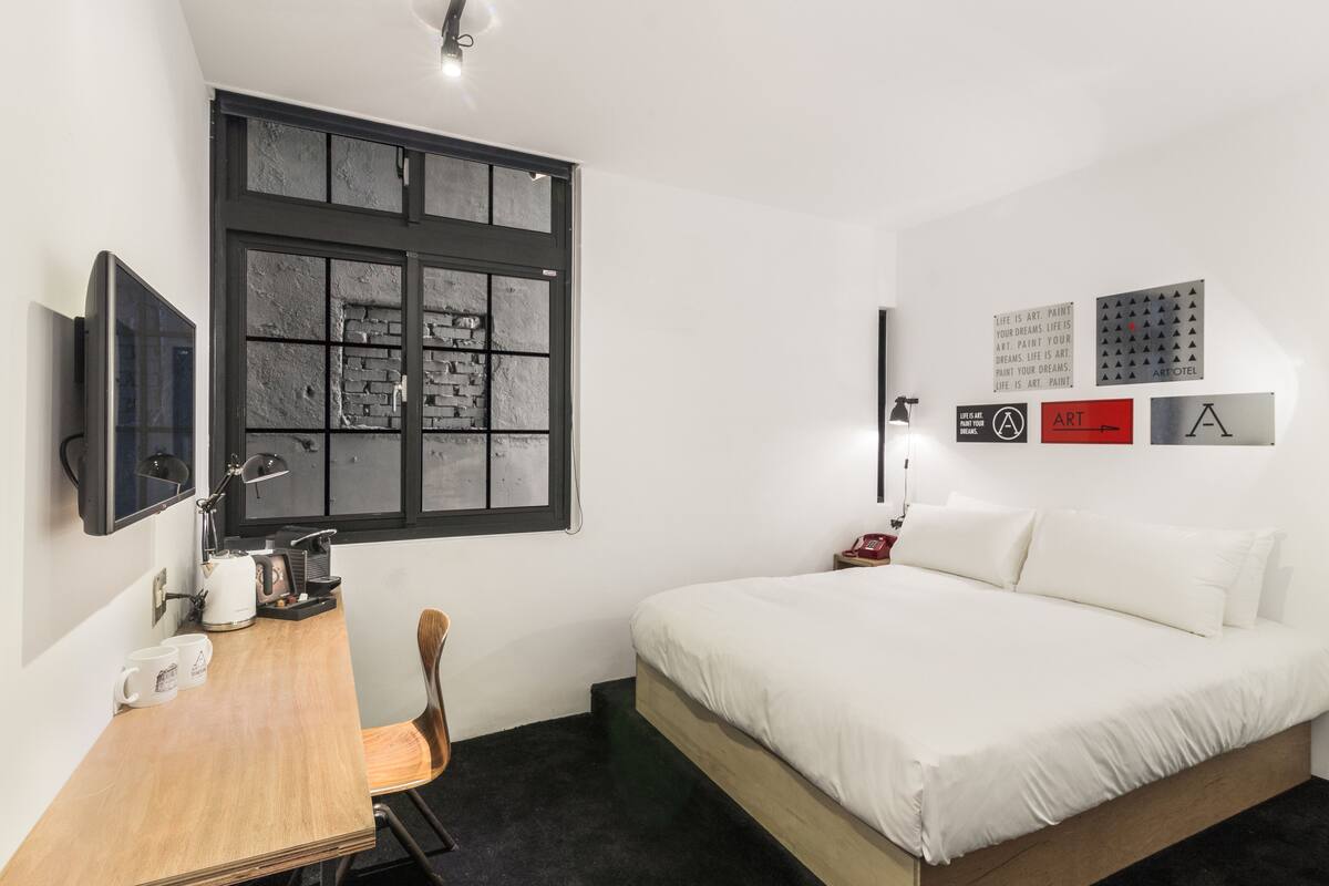 A hotel room with a bed, a desk with a chair, a coffee maker, and a television.