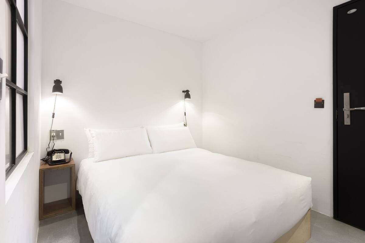 A hotel room with a bed, bedside lamps, a nightstand, a telephone, and a door.