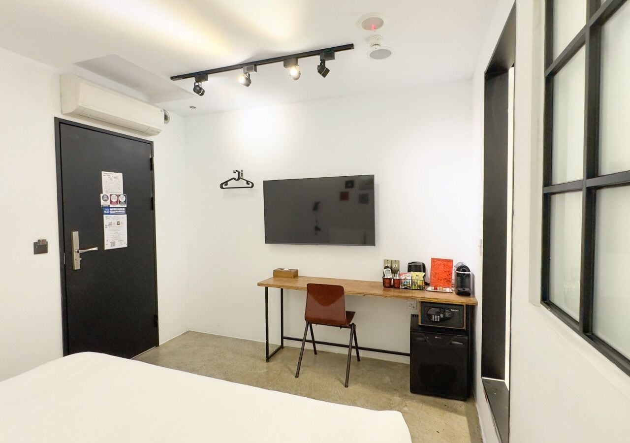 A small, clean room with a bed, a desk, a chair, a television, and a kitchenette.