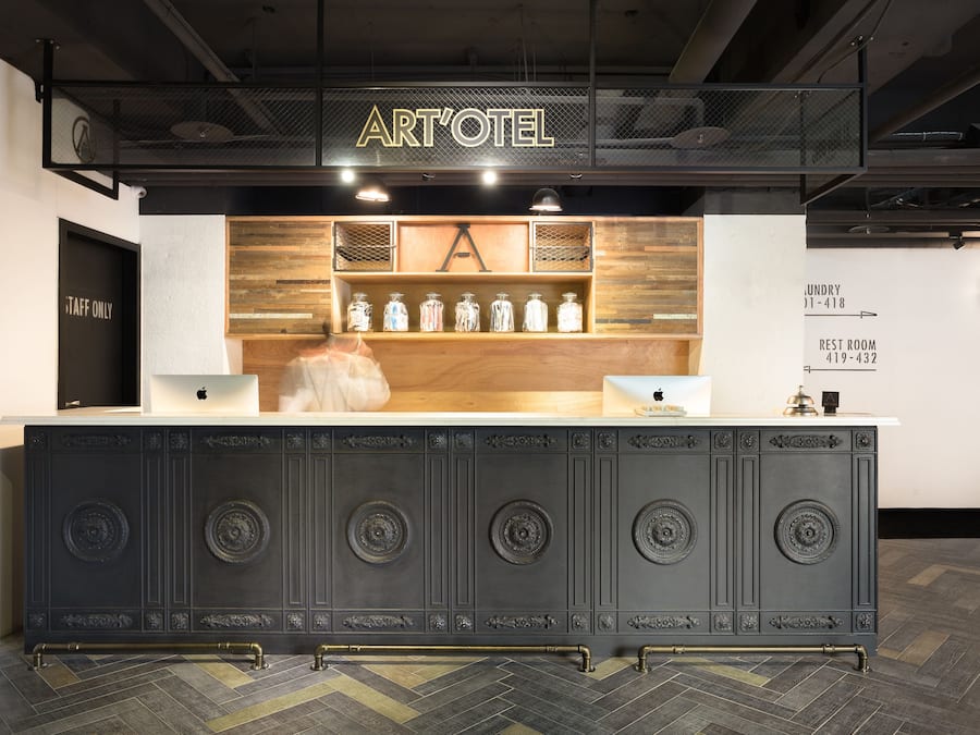 En receptionsdisk med et skilt der siger "ART'OTEL", en træhylde med krukker, og en dør med teksten "TAFF ONLY".