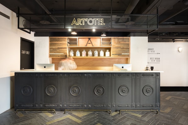 Una recepción con un letrero que dice "ART'OTEL", un estante de madera con frascos, y una puerta con la indicación "TAFF ONLY".