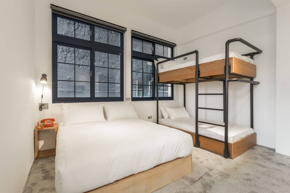A bunk bed room with a wooden frame, a single bed with white bedding, and a nightstand with a red telephone.