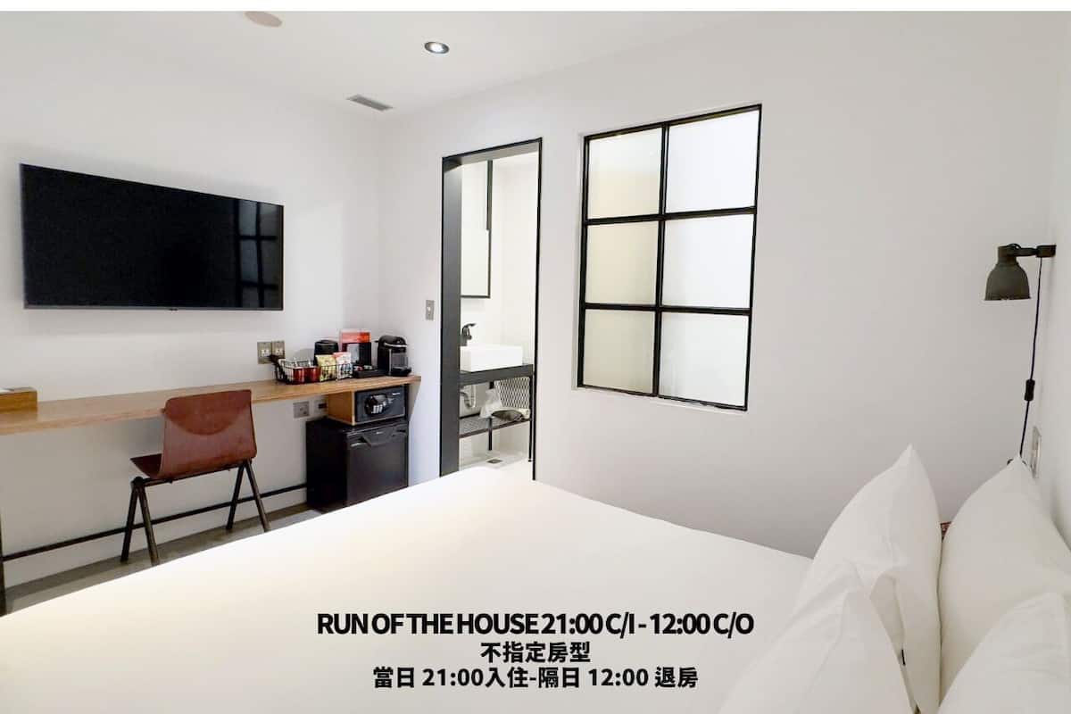 A modern hotel room with a bed, a desk, a chair, a TV, and a window with blinds.