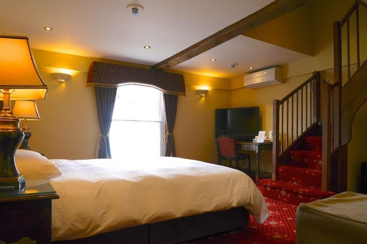 A hotel room with a bed, a desk, a television, and a staircase.