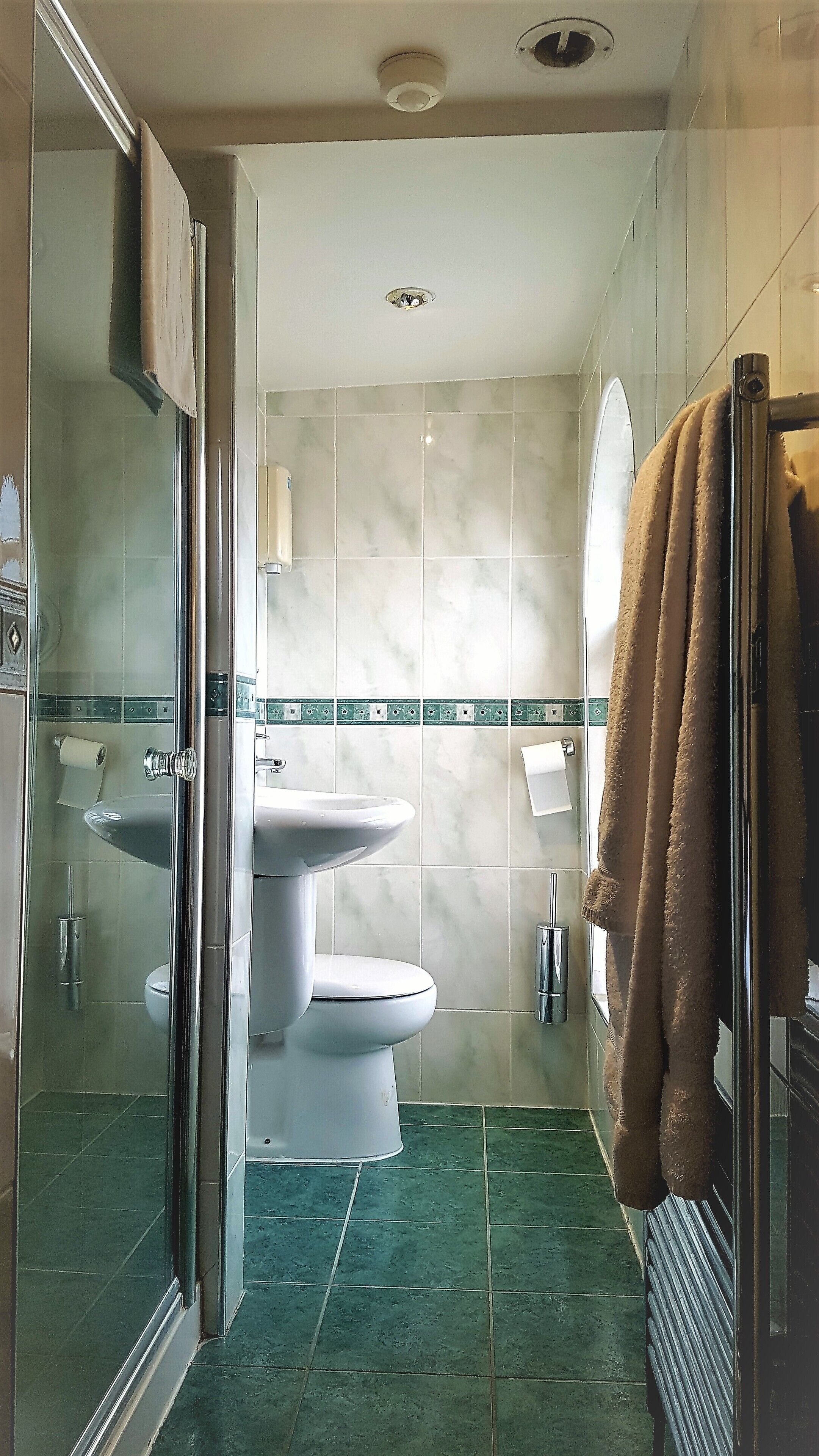 Un baño con mampara de vidrio, inodoro, lavabo y perchero para toallas.