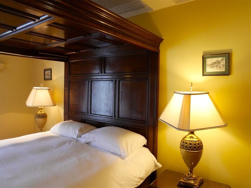 Ein Hotelzimmer mit einem hölzernen Kopfteil, zwei Nachttischlampen und einem gerahmten Bild an der Wand.