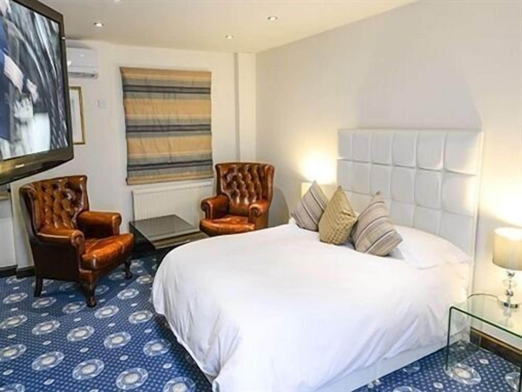 A hotel room with a large bed, two armchairs, a small table, and a TV mounted on the wall.